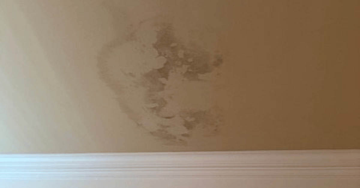 A water stain on a beige ceiling indicating a roof leak above.