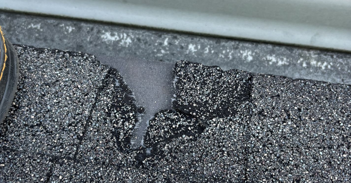 Close-up of a damaged roof shingle near a gutter, with visible wear.