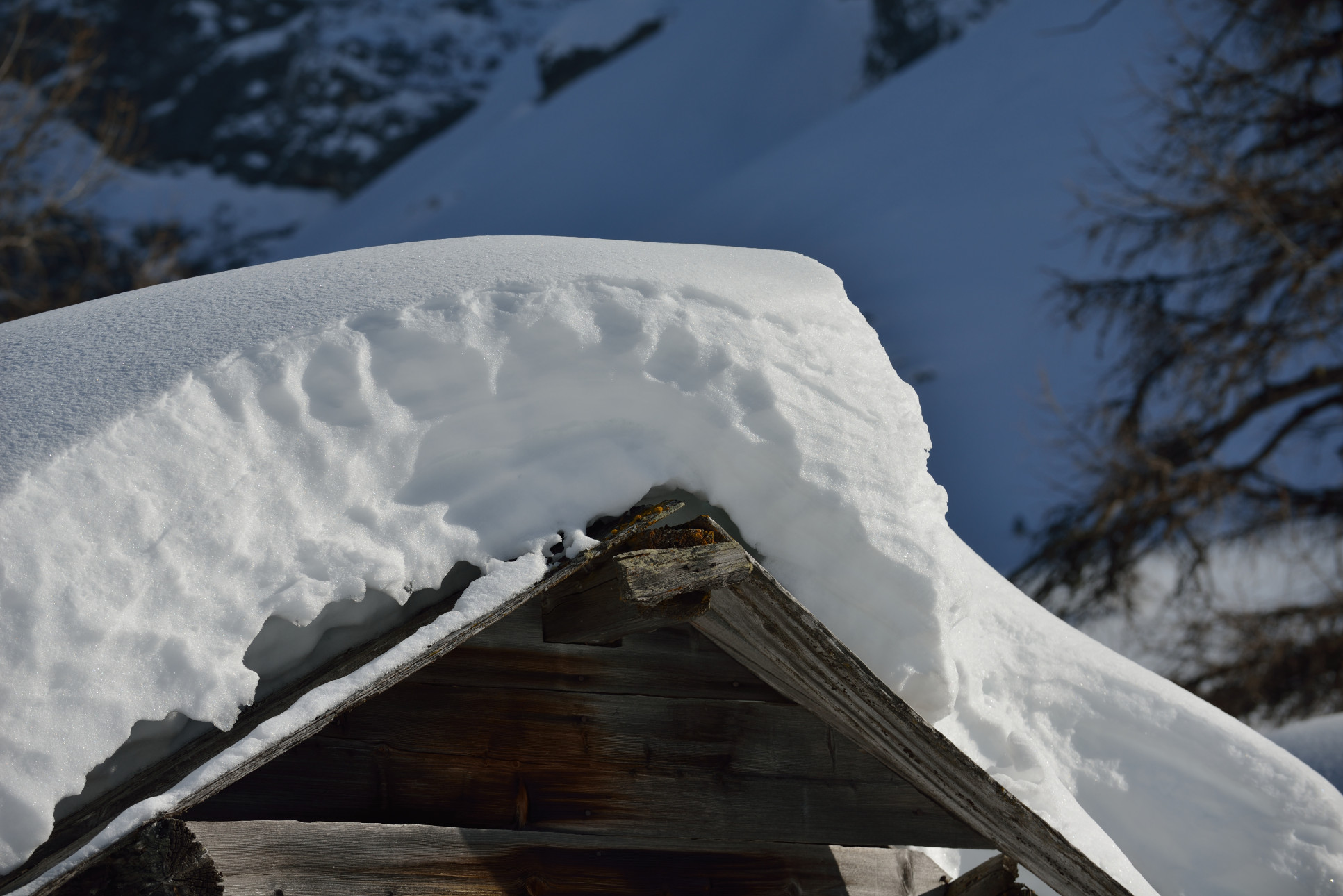 A house roof covered in thick snow against a clear blue sky.