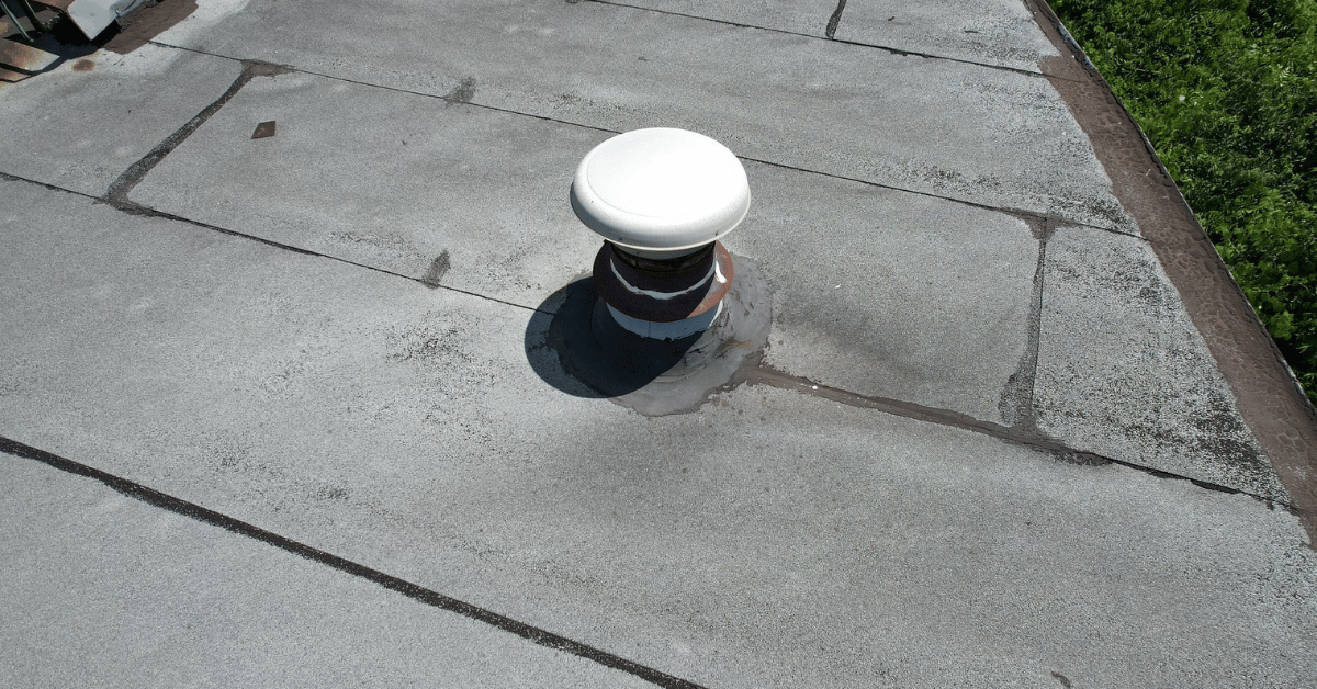 A close-up of a white vent pipe on a gray flat roof, showing careful sealing and professional craftsmanship.