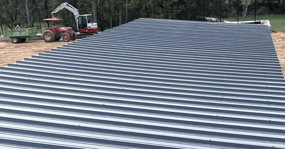 A metal roof under construction, featuring silver panels laid out with construction equipment in the background.