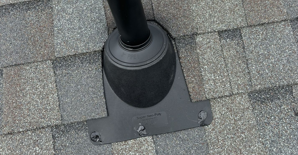 Close-up of a black pipe boot installed on gray roof shingles with a vent pipe emerging from the boot