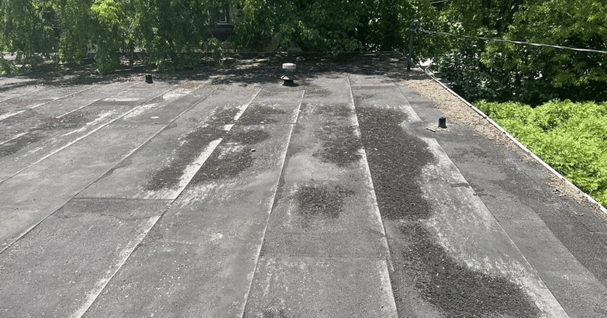 An aged flat roof showing wear and tear, with patches of debris and visible signs of deterioration.