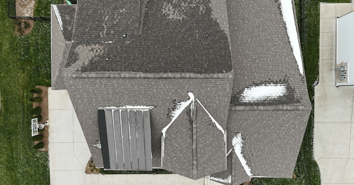 Top-down view of a snow-covered asphalt shingle roof with patterns indicating uneven snow melting.
