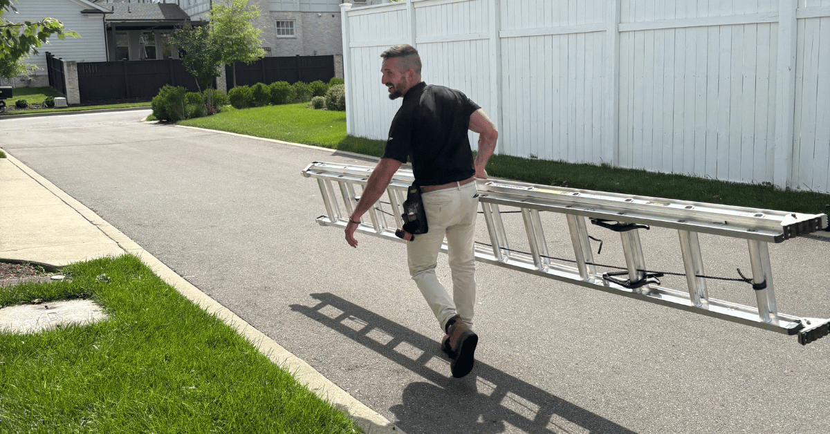 A roofer carrying a ladder down a suburban street, preparing for a roofing inspection.