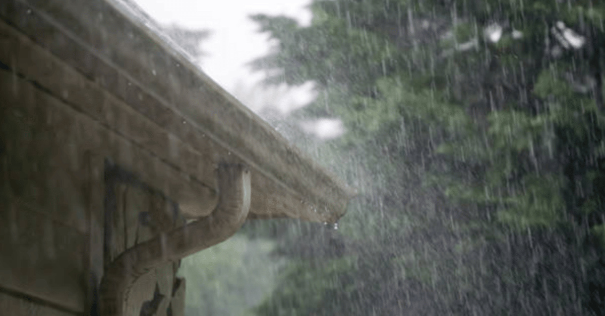 Close-up of rain spilling over gutters on a house during a storm, showing gutter overflow and water runoff issues.