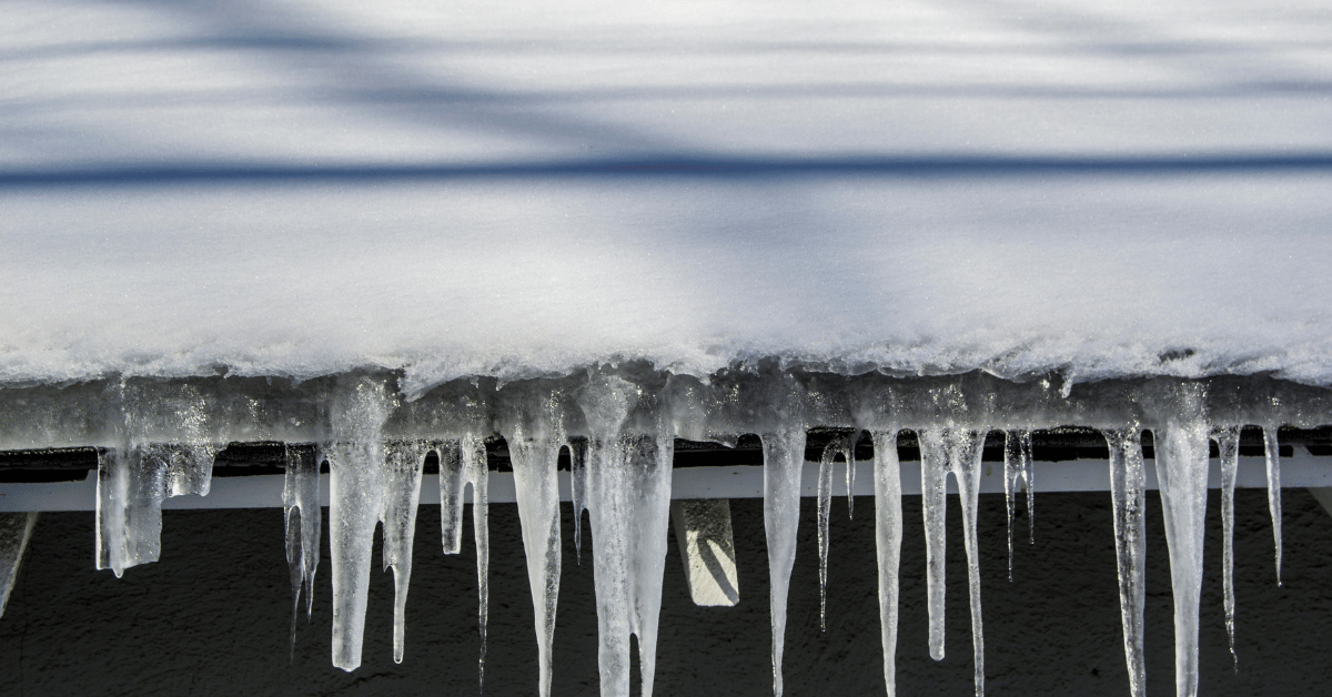 Large icicles hanging from the edge of a snow-covered roof and frozen gutters.