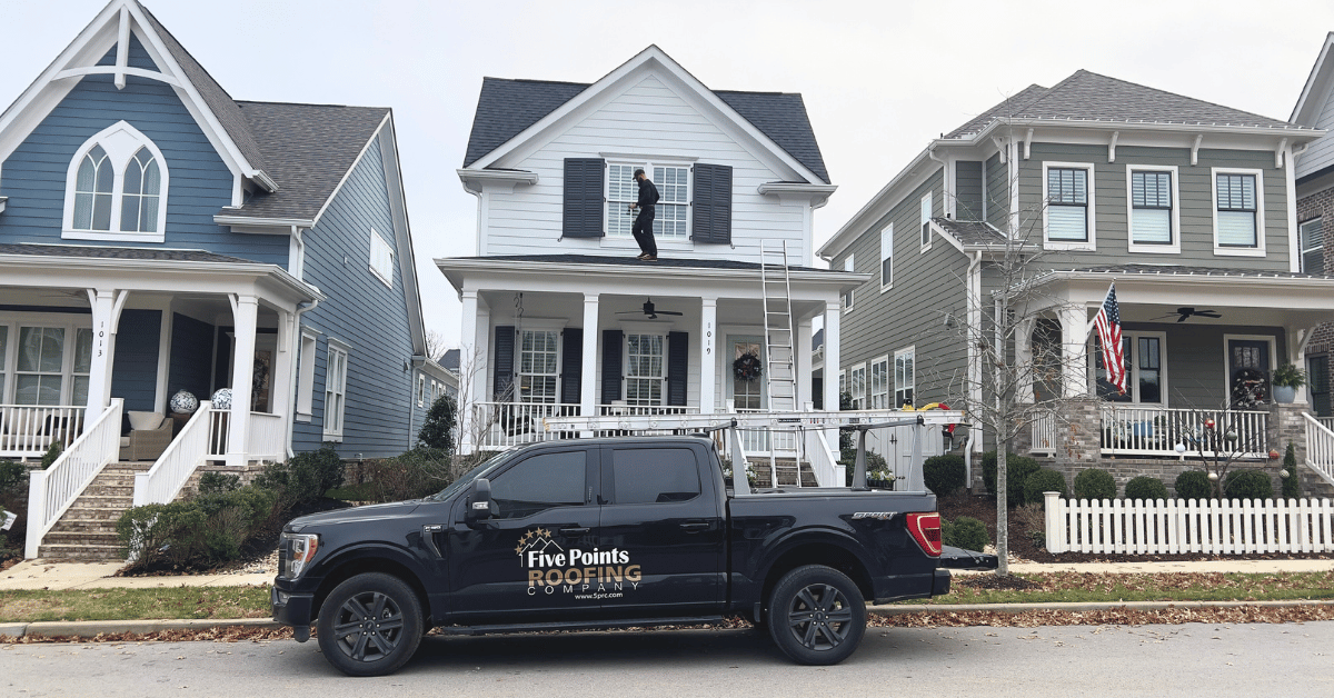 A roofing professional inspecting a two-story house roof with a black pickup truck parked out front.