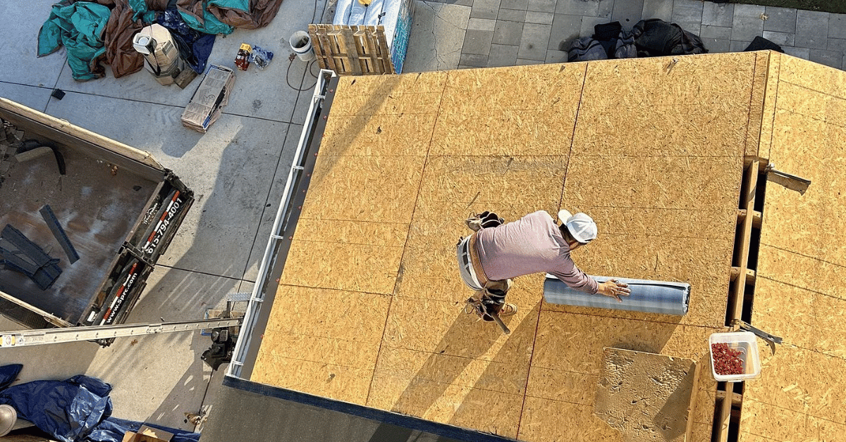 A roofing contractor installing underlayment on a wooden roof deck during a home construction project.