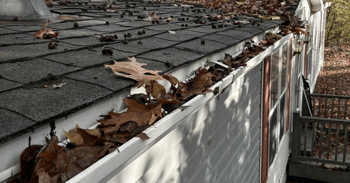A home’s roofline with gutters filled with dried leaves and small branches.
