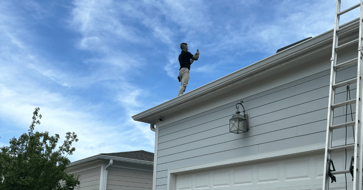 A roofer standing on a residential roof inspecting and documenting its condition.