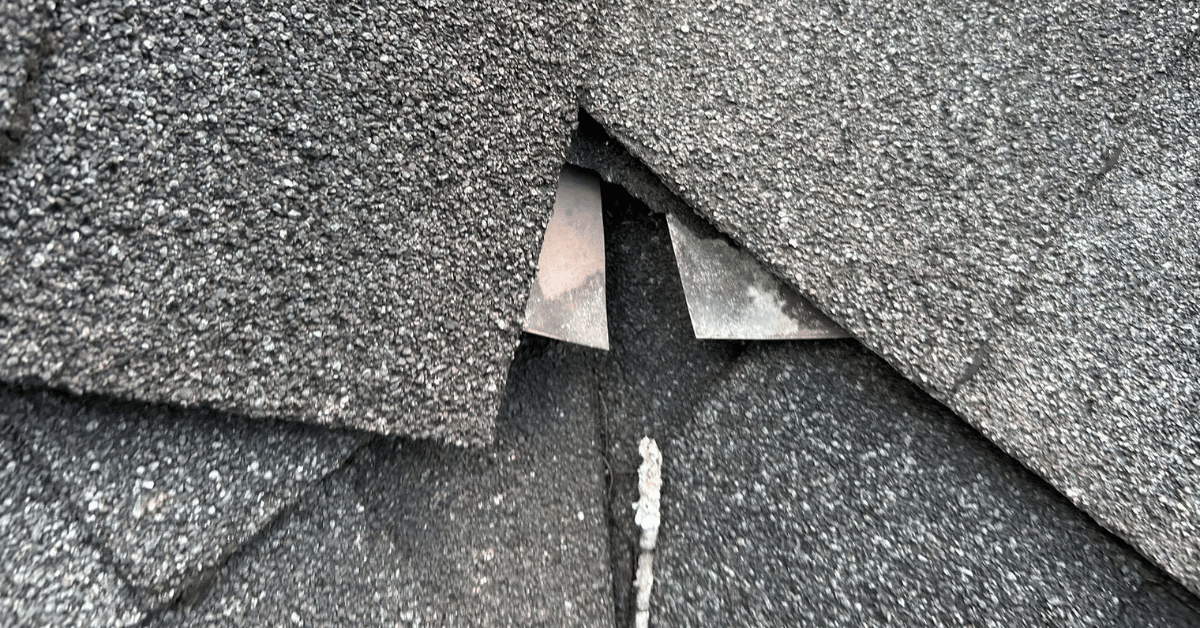 A close-up of torn shingles revealing the underlayer of the roof, indicating severe weather damage.