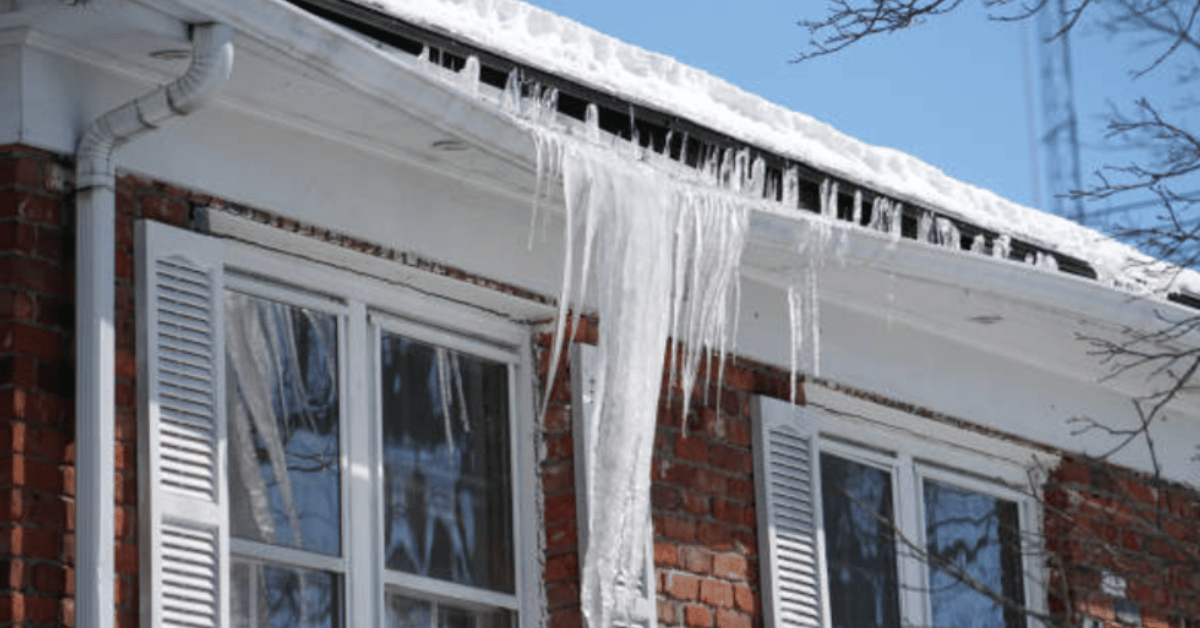 Icicles and ice dams forming along the edge of a home's roof during winter, potentially causing roof damage and leaks.