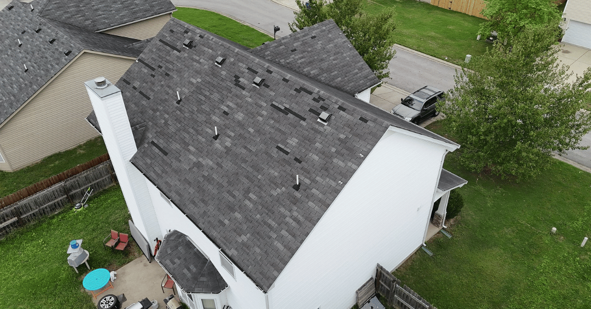Aerial view of a house with missing shingles on the roof caused by wind damage during a recent storm.
