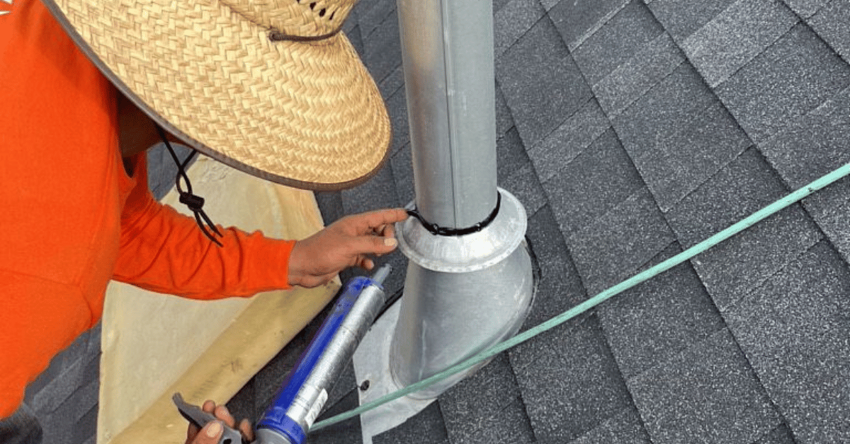 A roofing contractor applying sealant to the base of a pipe boot on a roof.