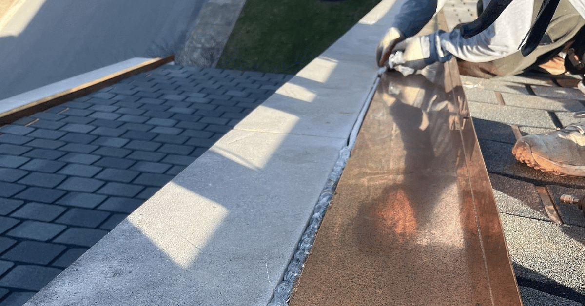 A roofer sealing copper flashing along a roof edge for superior weather resistance.