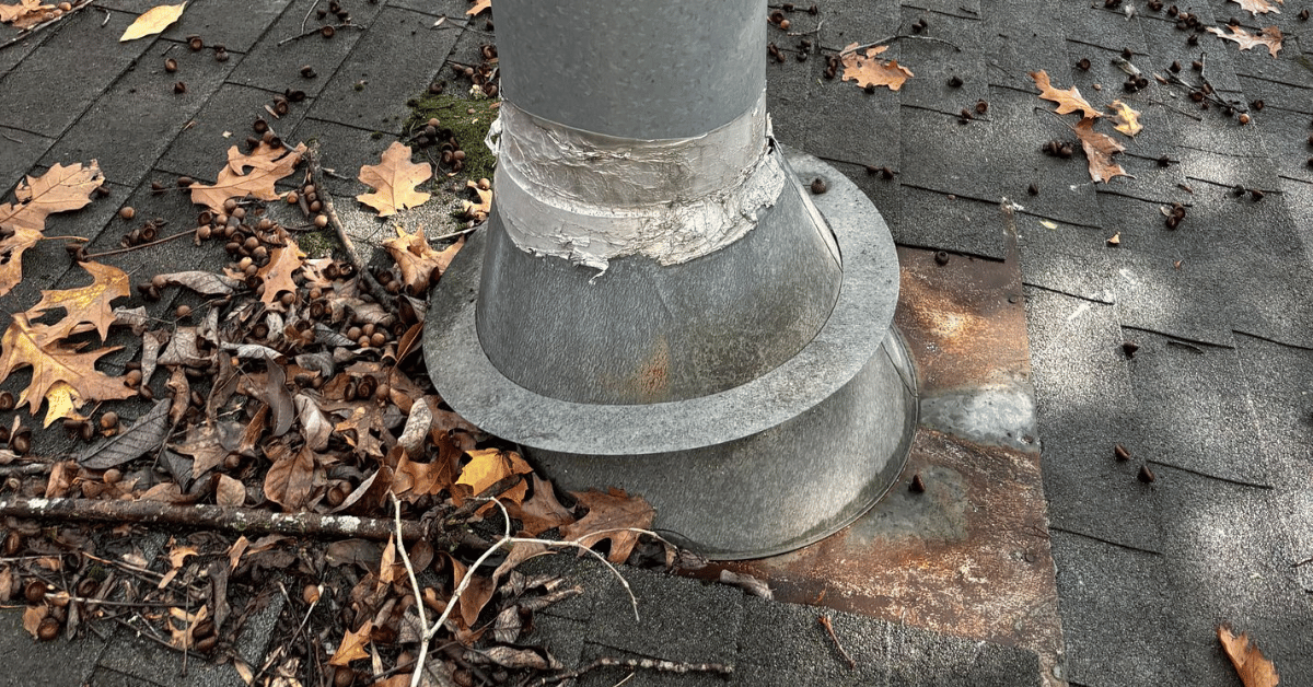 A metal pipe boot with visible damage and debris on a weathered roof.