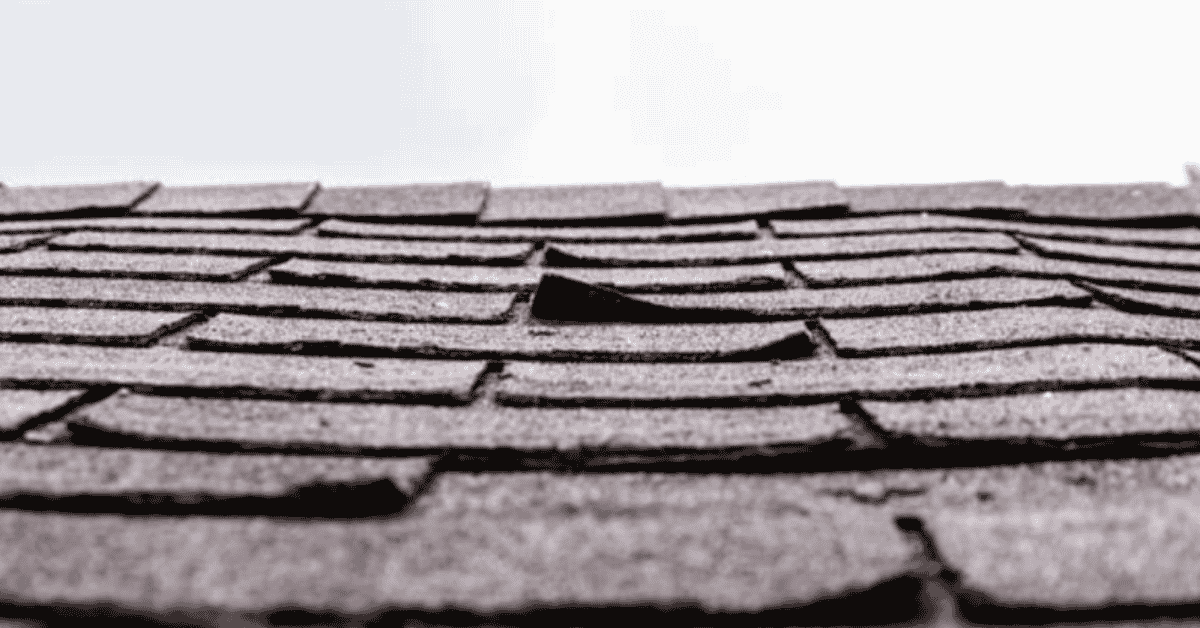 A close-up of curled and damaged shingles on a roof.