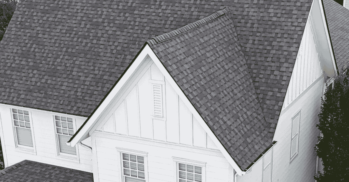 A close-up view of a white house with a gable roof featuring a steep slope and asphalt shingles.