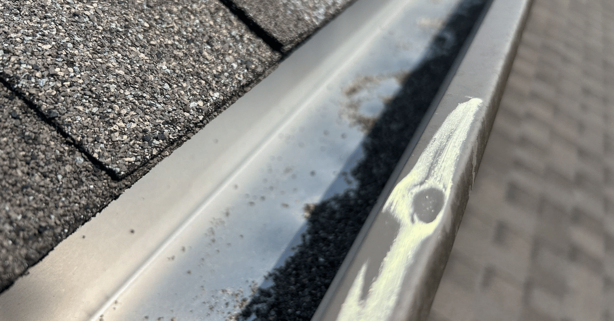 A close-up of a metal gutter with a dent and scuff marks caused by hail impact.