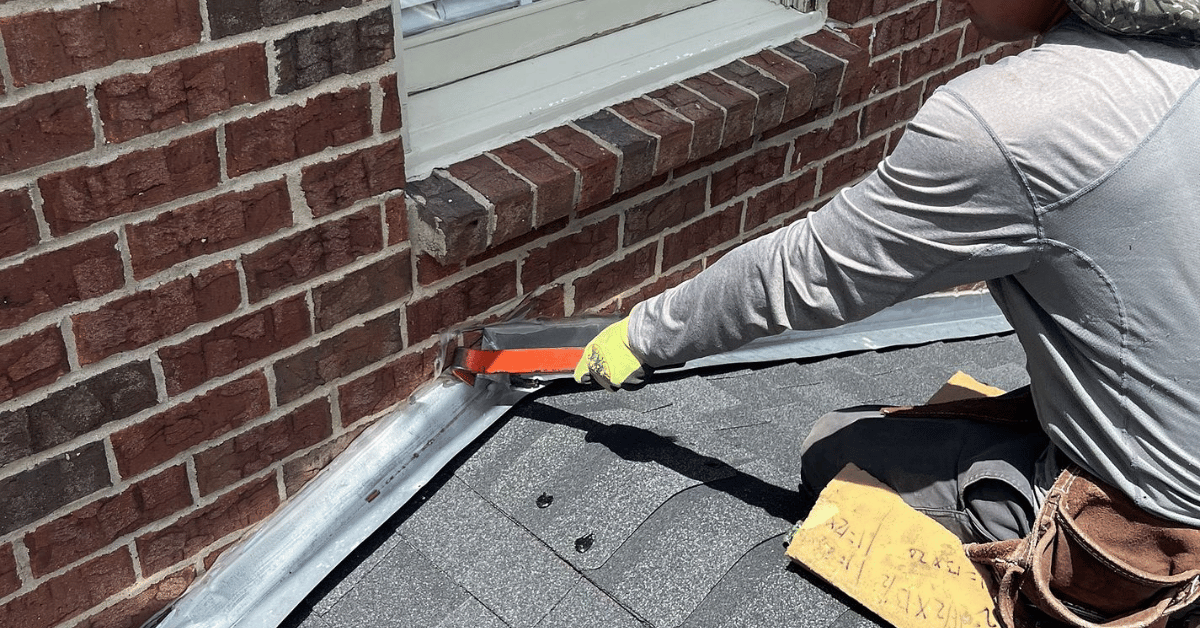 A roofer using a tool to inspect and repair metal flashing on a brick home.
