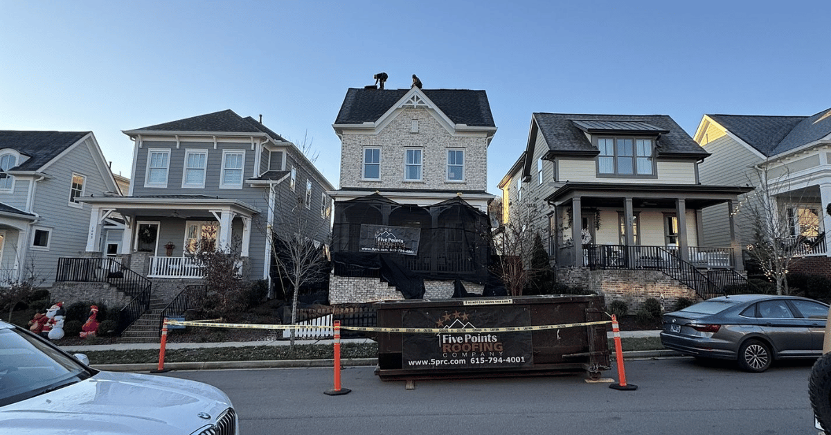 A home with ongoing roof installation, featuring protective netting and a dumpster for waste removal.