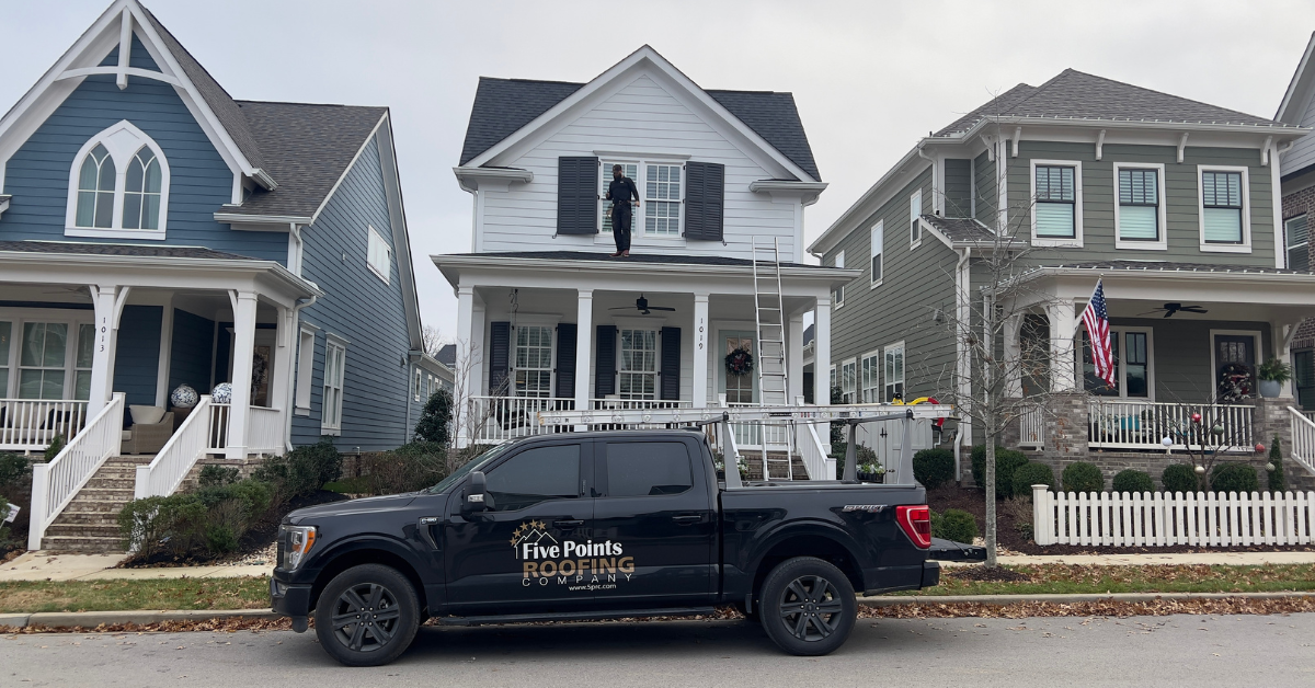 A Five Points Roofing truck parked in front of a house, with a professional roofer inspecting the roof.