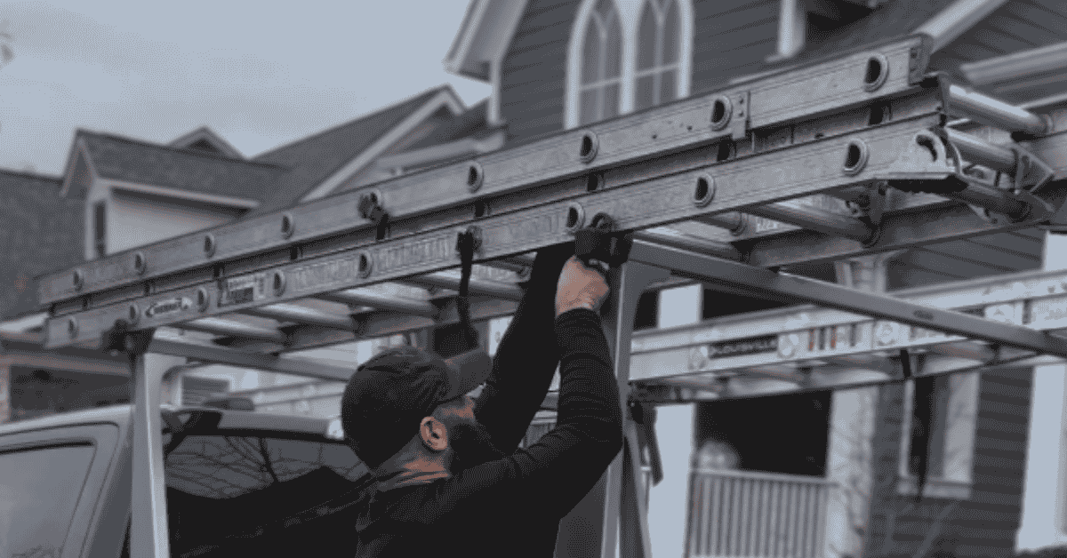 A roofer securing a ladder against a truck to prepare for a storm damage roof inspection.