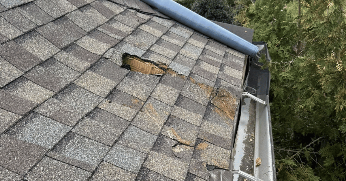 A residential roof with a large hole caused by fallen debris during a severe storm.