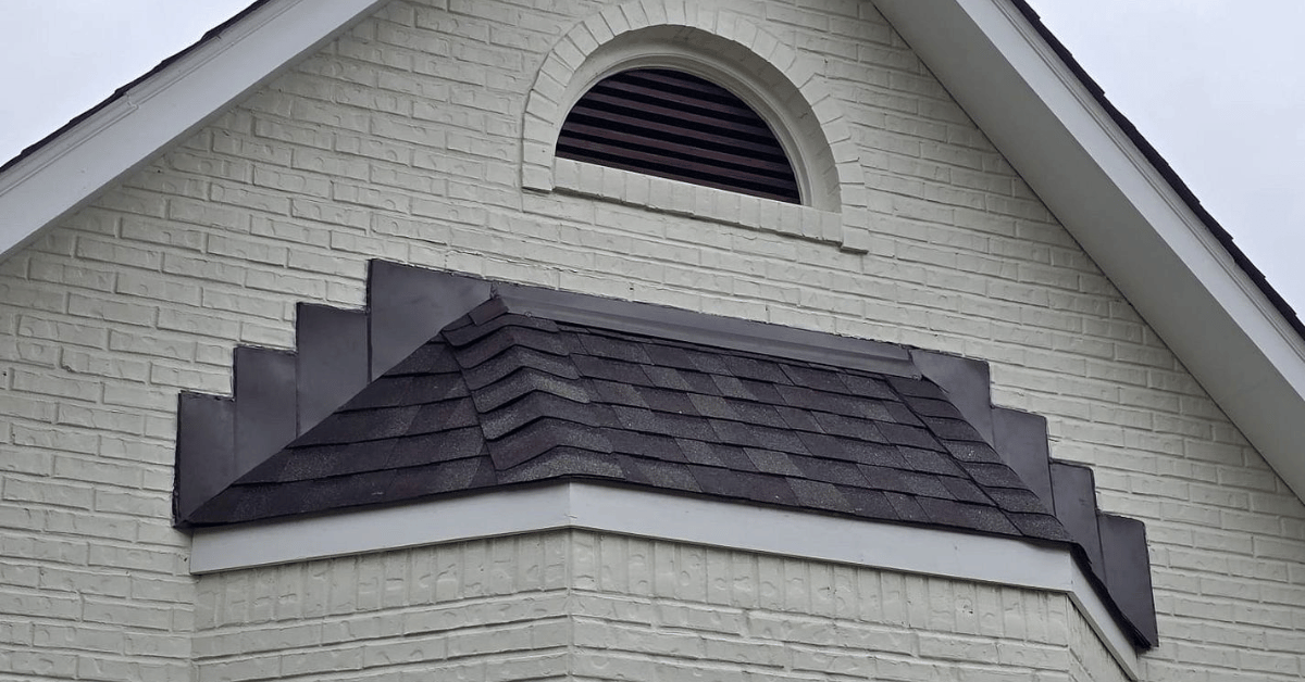 A gable roof with newly installed step flashing along a white brick wall.