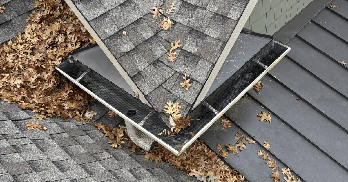 Gutters filled with leaves and debris piling up at roof junctions, causing water drainage issues.