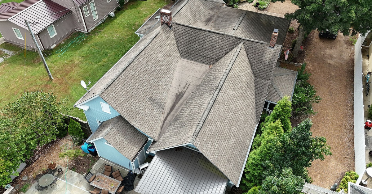 Aerial view of a home's asphalt shingle roof with dark stains and visible wear.