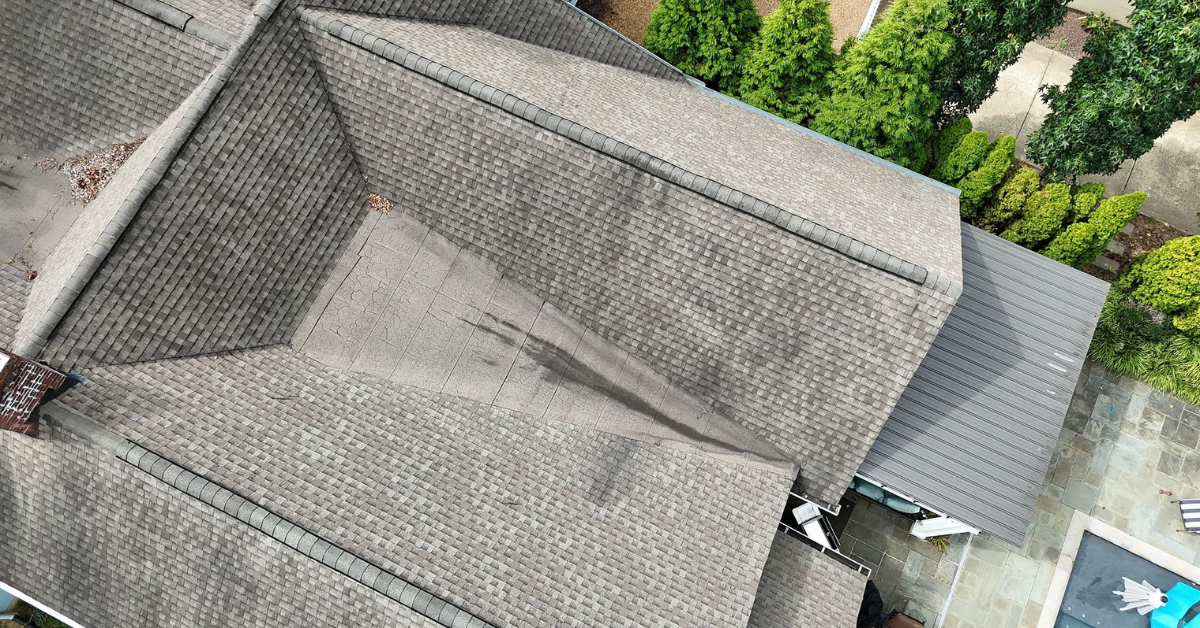 Aerial view of a house's roof showing dark stains and uneven shingle wear.