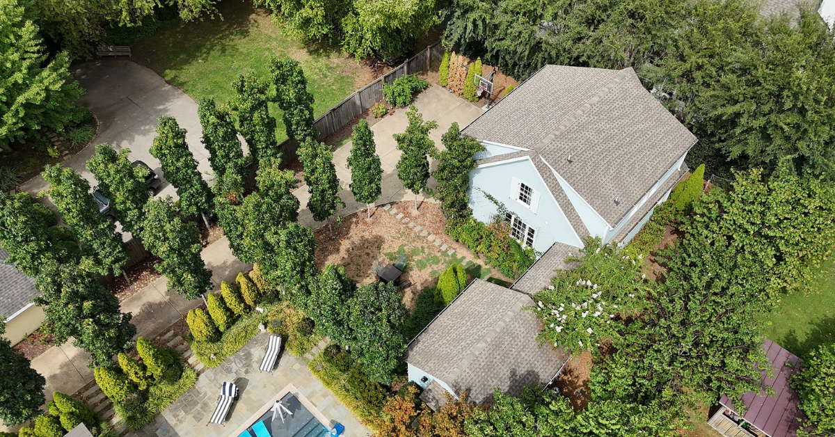 Aerial view of a home with an asphalt shingle roof surrounded by trees and a backyard.