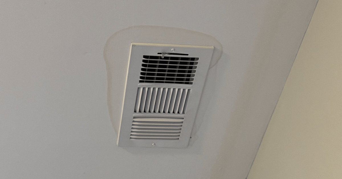 Water stain forming around a ceiling air vent due to excess moisture.