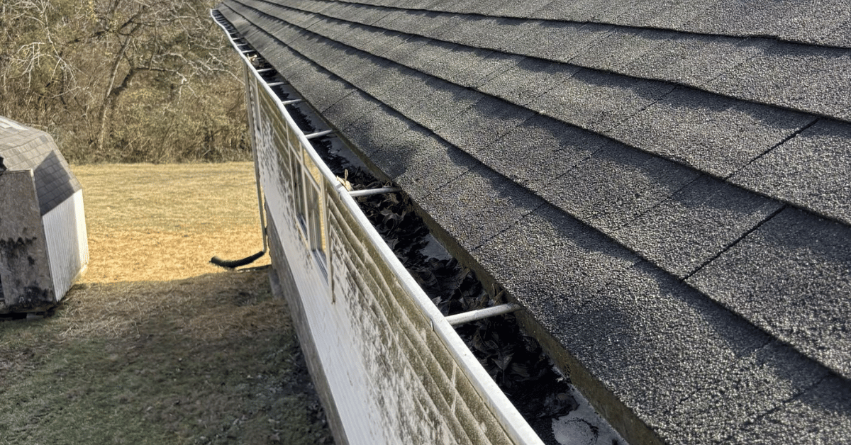 A roof with clogged gutters filled with leaves and dirt.