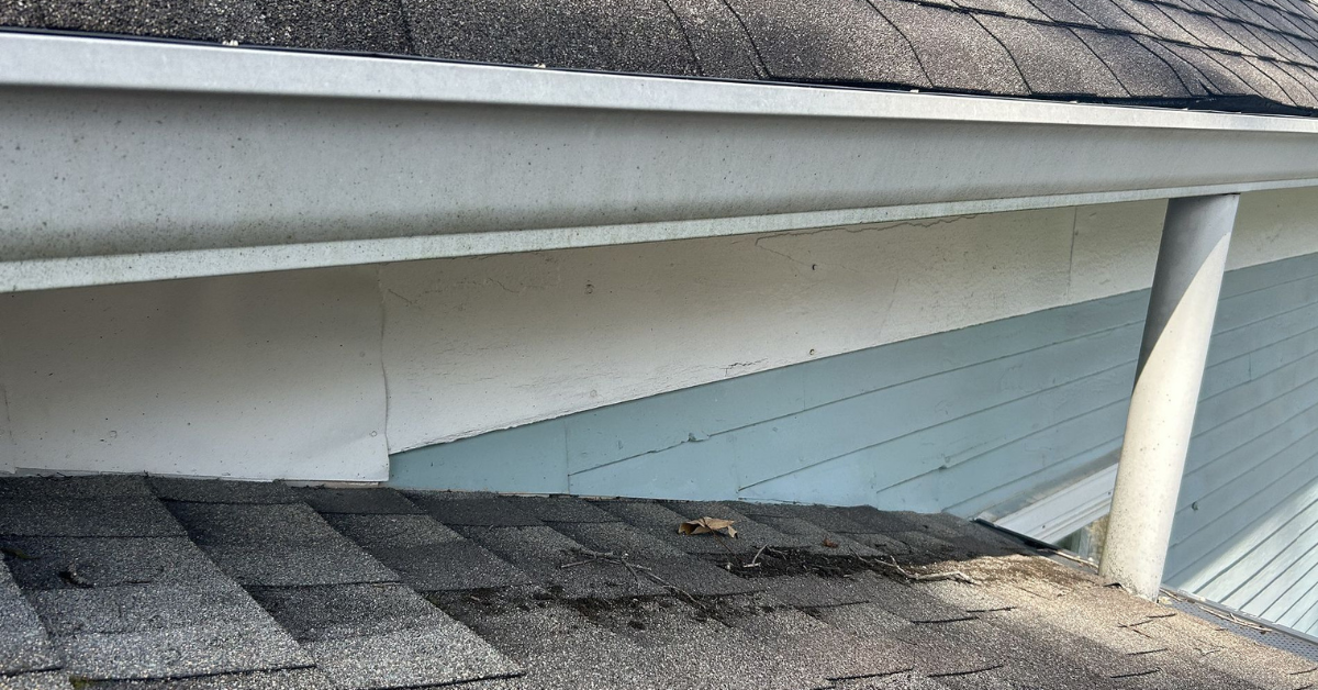 Close-up of a roof edge with white gutters and visible cracks in the house's siding.