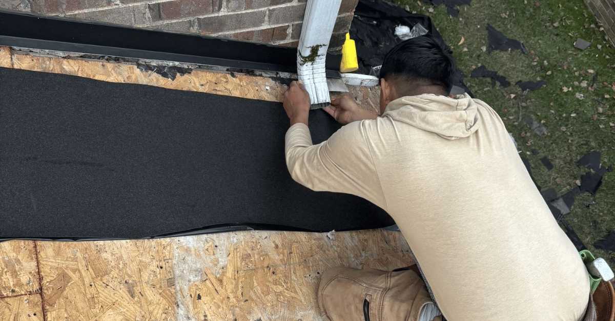 A roofing contractor securing a waterproof underlayment near the edge of a home's roof.