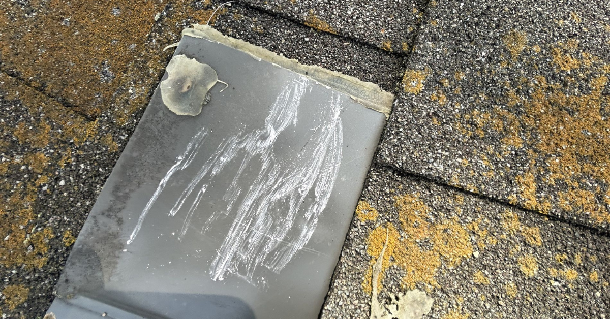 A metal flashing piece with scratches and visible algae growth on the surrounding shingles.