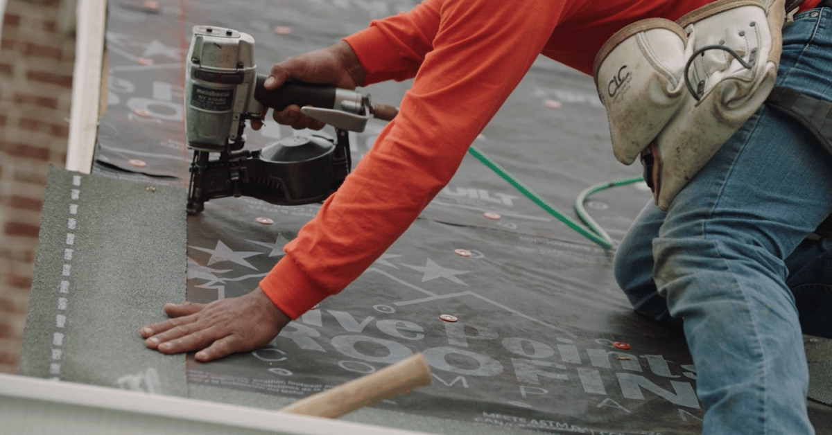 Roofing Questions: A Five Points Roofing professional roofer in an orange shirt installing high-quality roofing underlayment.
