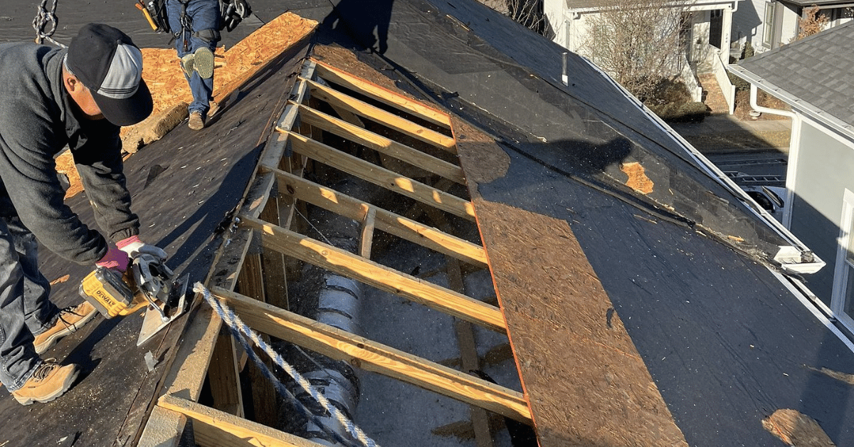 Roofing professionals repairing exposed wooden roof decking during a roof replacement.