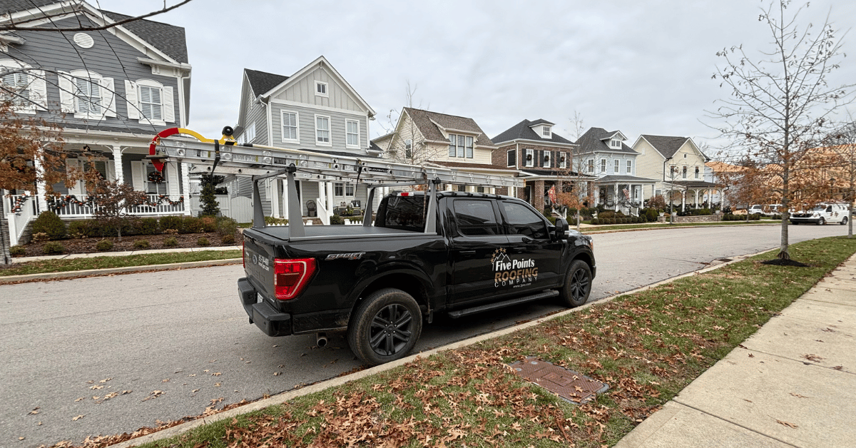 A black Five Points Roofing company truck parked on a suburban street in front of homes.