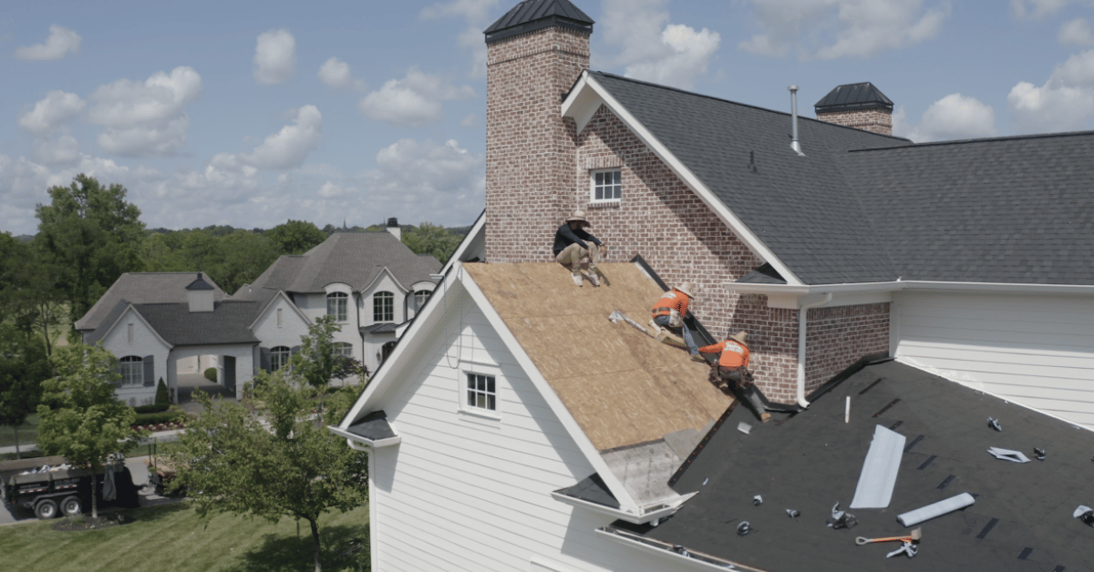 A team of roofers working on a steep-pitched roof, replacing old shingles with new materials.