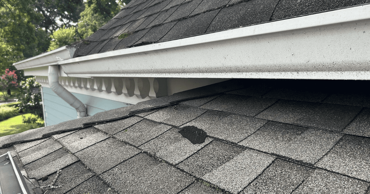 Loose and damaged asphalt shingles near the gutter line, with some missing pieces.