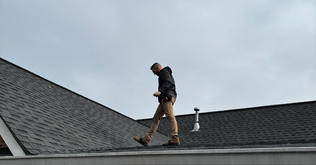 A roofing contractor walking on a residential roof while carrying inspection tools.
