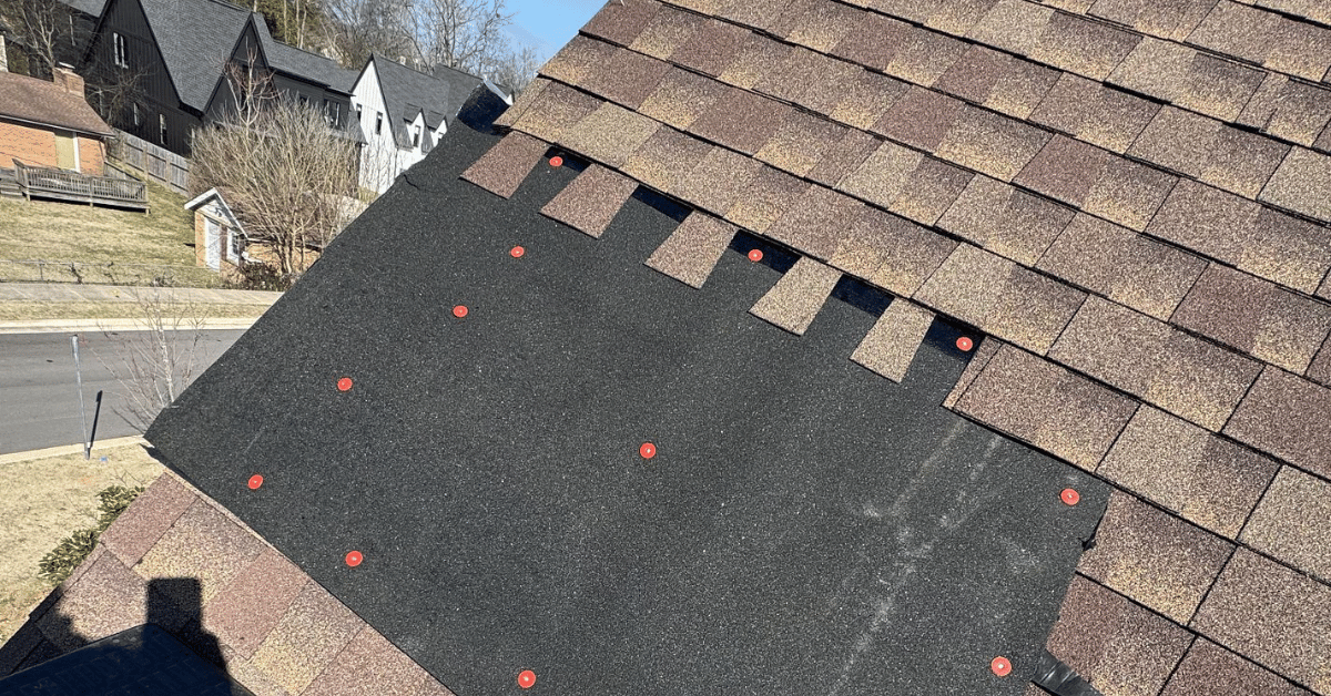 A partially installed roof with visible synthetic underlayment secured with red fasteners.