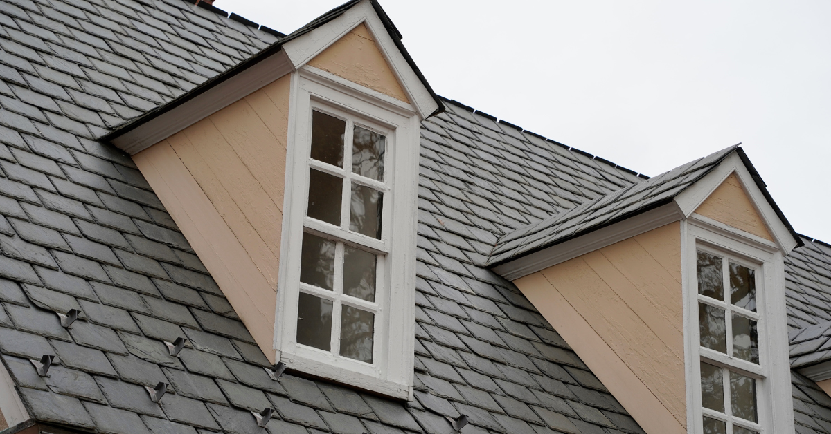 A close-up of a gray slate tile roof with two dormer windows.