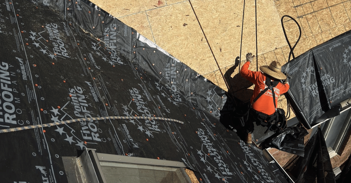 A Five Points Roofing contractor wearing safety gear, installing underlayment with Five Points Roofing branding.