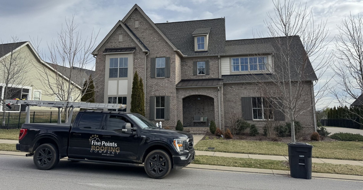 A Five Points Roofing Company truck parked in front of a two-story brick home.