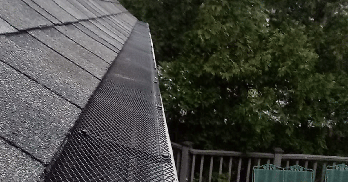 A close-up of a black gutter guard installed on a shingle roof.